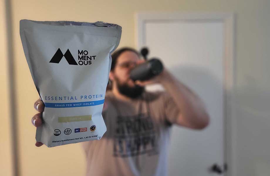 Olympian Caine Wilkes holds up a bag of Momentous Whey Protein while drinking a shake in the background.