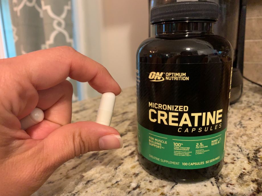 A person holds a capsule next to a bottle of Optimum Nutrition Creatine