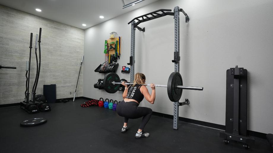 A woman performs back squats while using the PRx Profile Folding Squat Rack