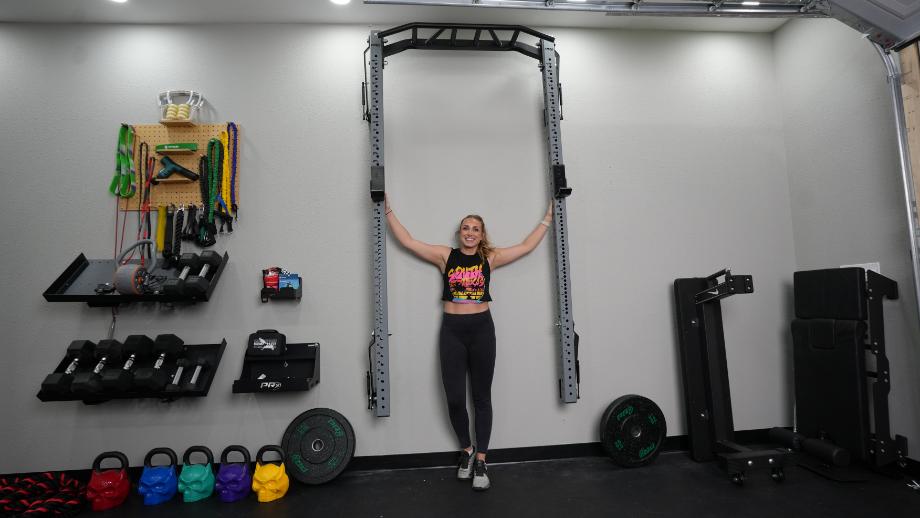 A woman stands underneath a folded PRx Profile PRO Squat Rack