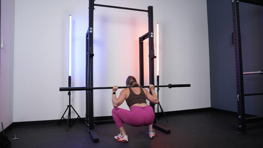 A woman squatting on the Rogue HR-2 Half Rack with blue and orange light bars against the wall on either side of the rack