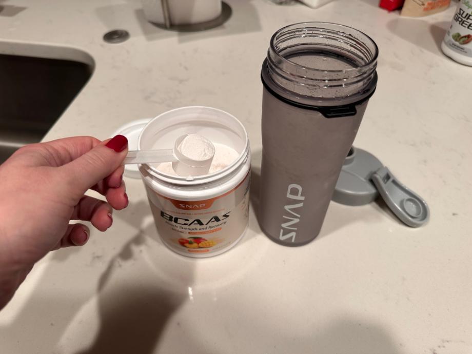A person taking out a scoop of Snap Supplements BCAA Powder from the container
