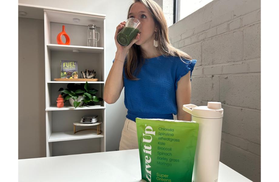 Woman drinking Live it Up Super Greens from a clear cup. The liquid is a dark green.